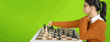 a woman in an orange sweater is playing a game of chess on a green screen .