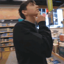 a young man in a black sweater is standing in a store looking up at the ceiling