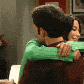 a woman in a green sweater hugs a man in a brown shirt