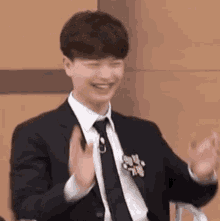a young man in a suit and tie is sitting in a chair and clapping his hands .