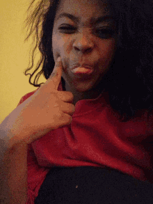a woman in a red shirt is making a funny face with her finger in her mouth