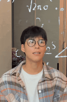a man wearing glasses and a plaid shirt stands in front of a chalkboard that says " v2no "
