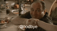 a man is sitting at a table with a bottle of wine and a plate of food and says goodbye