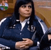 a woman in a blue jacket is sitting in a chair with her hands on her chest .