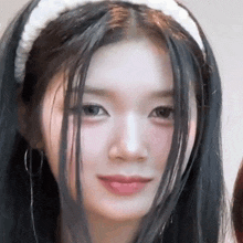 a close up of a woman with long black hair wearing a white headband .