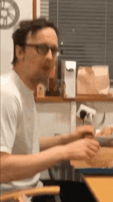 a man wearing glasses is sitting at a table with a plate of food in front of him .