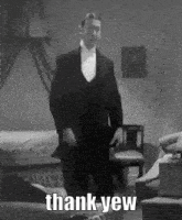 a man in a tuxedo and bow tie is standing in a room with the words `` thank yew '' written on it .