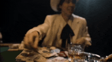 a man in a cowboy hat is sitting at a table with a glass of whiskey and cards .