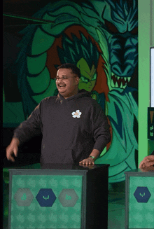 a man wearing a black hoodie with a flower on the front stands in front of a dragon ball mural
