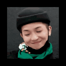a young man wearing a black hat and a green scarf is smiling and holding a stuffed animal .
