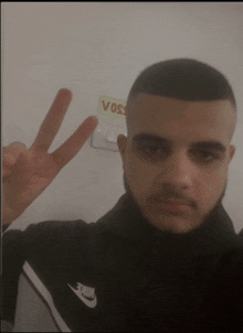 a man giving a peace sign in front of a sign that says " voss "