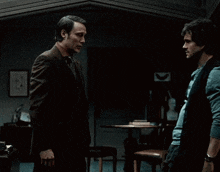 two men are standing next to each other in a dark room and looking at each other