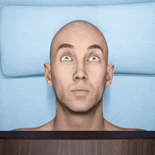 a bald man with a surprised look on his face laying on a bed