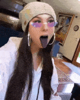 a woman wearing a beanie and purple sunglasses is sticking her tongue out .