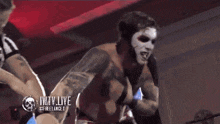 a shirtless man with white paint on his face stands in front of a sign that says wtv live