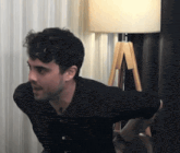 a man in a black shirt is stretching his arms in front of a lamp