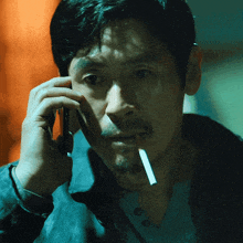 a man with a cigarette in his mouth talking on a cell phone