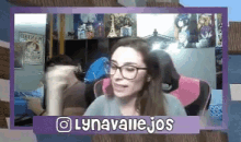 a woman wearing glasses is sitting in a pink chair in front of a purple frame with the words lynavalejos on it .