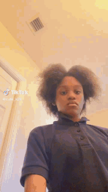 a young girl with curly hair is wearing a blue polo shirt and making a funny face .