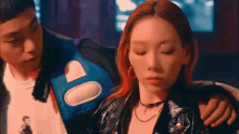 a man and a woman are standing next to each other . the woman is wearing a leather jacket and a choker .