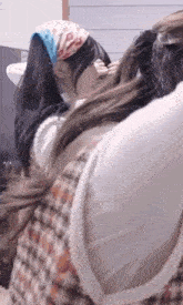 two women are standing next to each other in front of a sink . one of the women is wearing a bandana on her head .