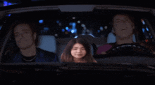 three people are sitting in a car with a girl in the back