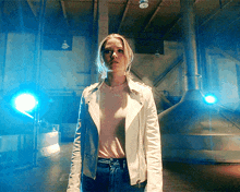 a woman in a white jacket stands in a dark room with blue lights