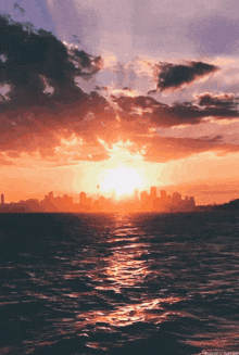 a sunset over the ocean with a city in the distance