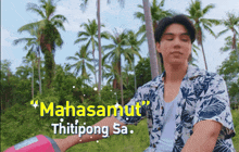 a man in a floral shirt stands in front of palm trees and the words mahasamut thitipong sa.