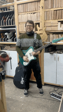a man in a green sweater is holding a guitar in a gibson case