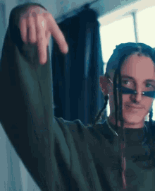 a man with dreadlocks is wearing a green sweater and giving a thumbs up