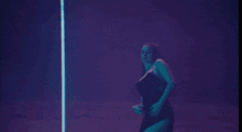 a woman in a black dress is dancing on a pole in the dark .