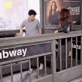 a man and a woman standing in front of a subway sign