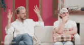 two men are sitting on a couch with their arms in the air
