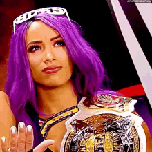 a woman with purple hair is wearing a crown and holding a wrestling championship belt .