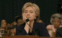 hillary clinton is sitting at a table with her hand on her face .