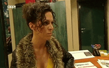 a woman in a fur coat is sitting at a desk with a sign that says jogoros