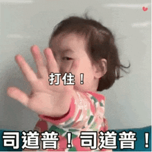 a little girl is making a stop sign with her hand in a foreign language .