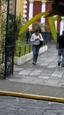 a woman is walking down a sidewalk while looking at her phone