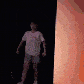 a girl in a white shirt and shorts is standing in front of a red wall .