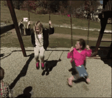 two girls are swinging on a swing set at a park .