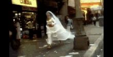 a woman in a wedding dress is walking down the street in front of a camera store