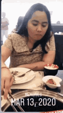 a woman is sitting at a table with plates of food and a bowl of rice .