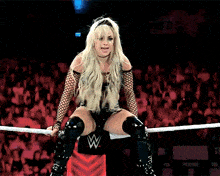 a woman is sitting in a wrestling ring with a w logo on the wall behind her