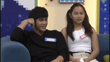 a man and a woman are sitting on a couch and the man has the name jarren on his shirt