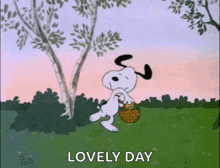 snoopy is walking in a field with a basket and a tree in the background .