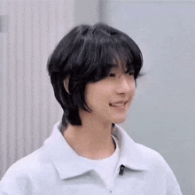 a young man with short black hair is smiling and wearing a white shirt .