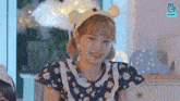 a young girl wearing a bear headband and a floral dress is smiling .