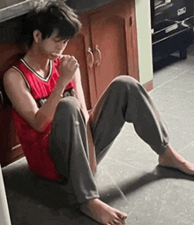 a young man is sitting on the floor in a kitchen eating a spoonful of food .