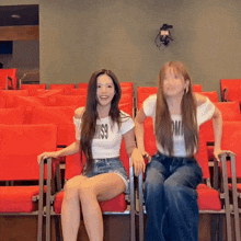 two women are sitting in red chairs with one wearing a white shirt that says miss9